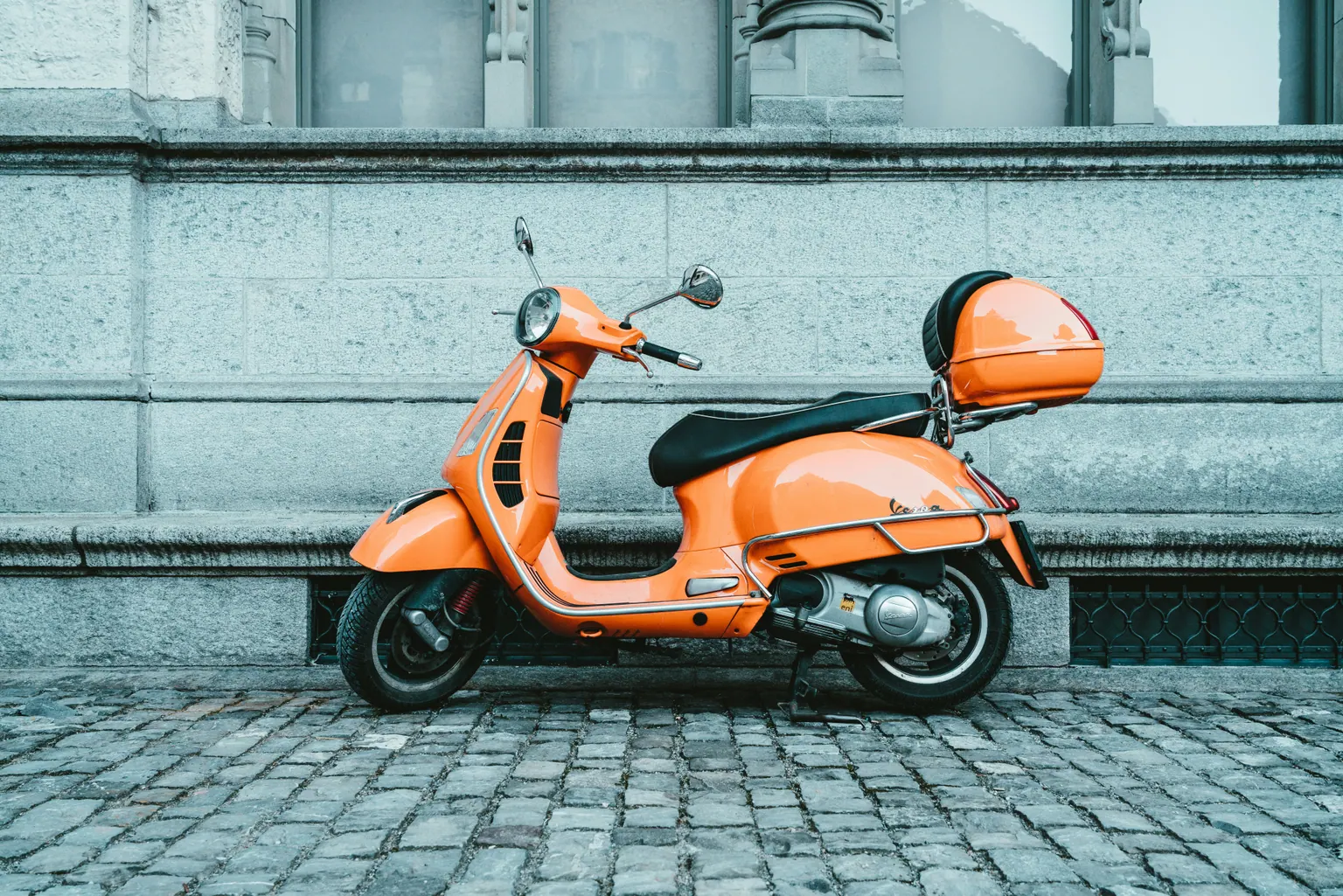 Scooter orange garé le long d’un mur turquoise
