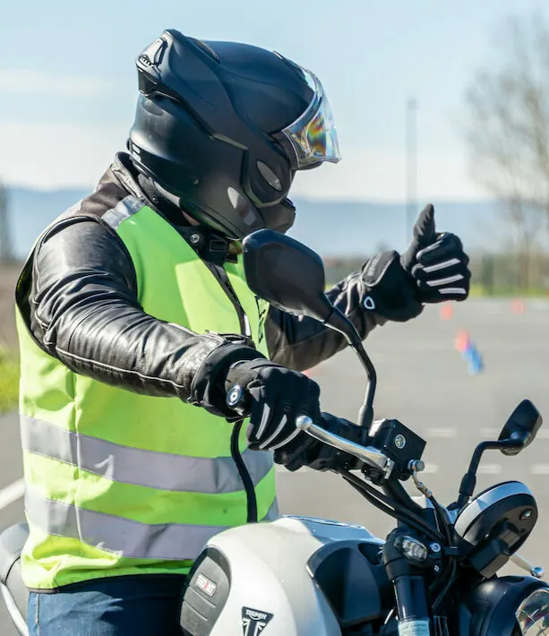 Élève moto casqué levant le pouce au guidon de sa moto école